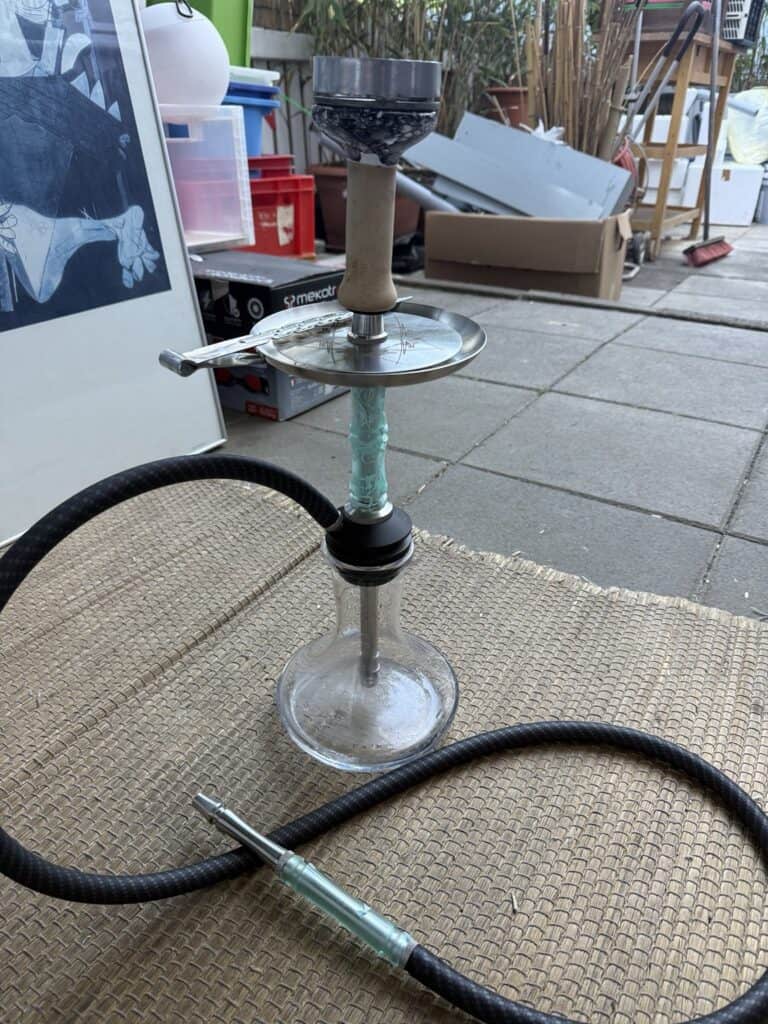 Alte Shisha mit Glasbowl und Schlauch auf Boden.