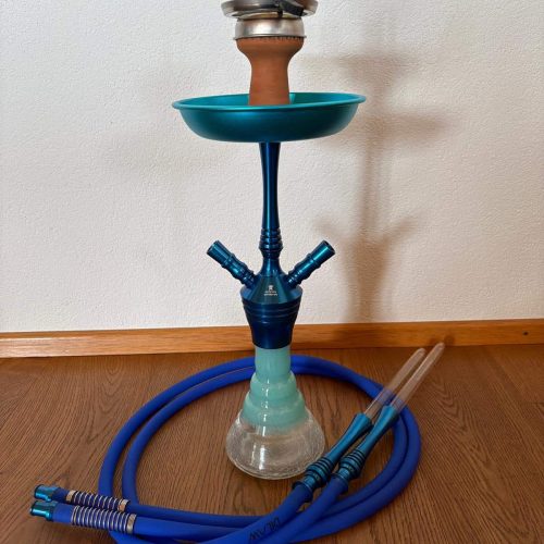 Shisha mit blauer Silikonschlauch und Zubehör, auf Holzboden vor weißer Wand.