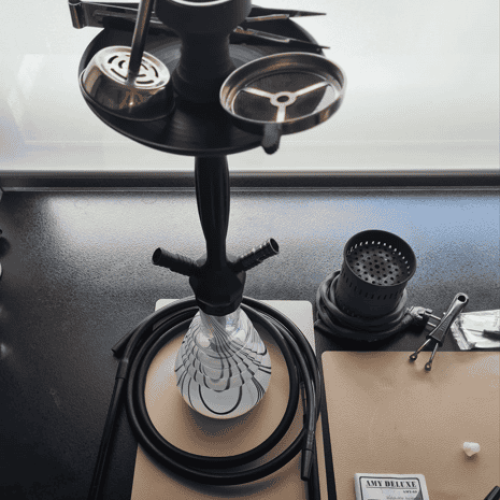 Shisha mit Glasbowl, Schlauch und Zubehör auf Tisch.