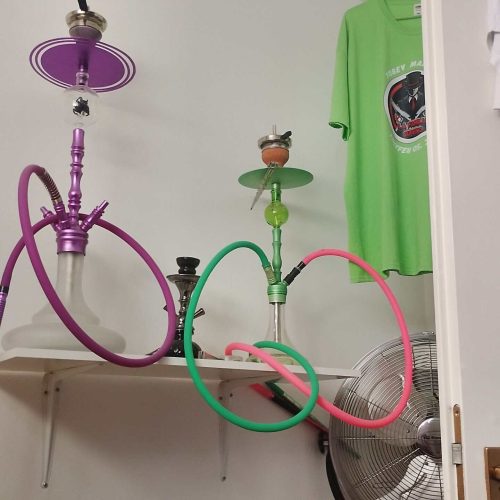Bunte Shisha mit grünen und pinken Schläuchen, auf einem weißen Regal.