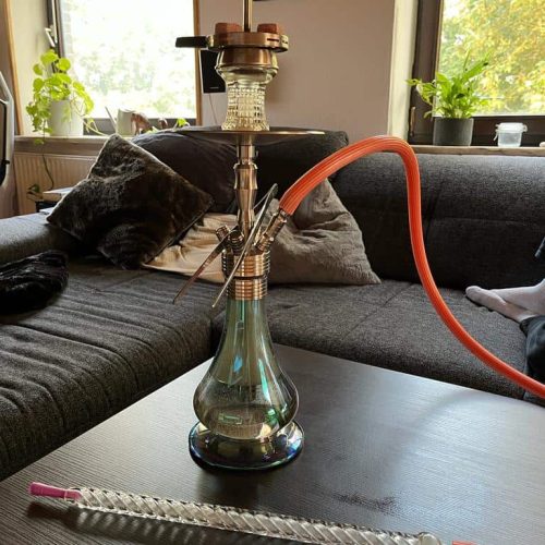 Rauchsäule mit Schlauch auf einem modernen Wohnzimmer-Couchtisch, umgeben von Kissen und Pflanzen.