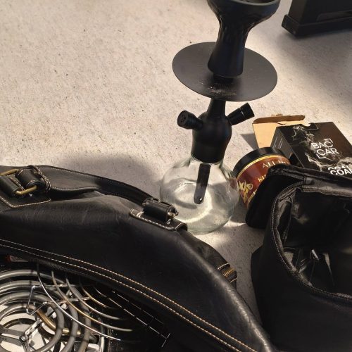 Shisha mit Glas, Schlauch und Zubehör auf Boden.