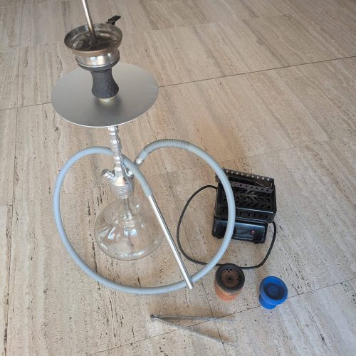 Rauch-Hookah mit Glas, Metall und Zubehör, auf Holzboden.