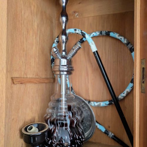 Shisha mit Glasbowl, Schlauch und Mundstück im Holzschrank.