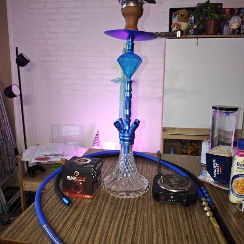 Rauchsäule mit Wasserpfeife, Schlauch und Zubehör auf Tisch, für Shisha-Liebhaber.