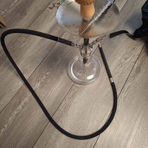 Shisha mit Glasbowl, Schlauch und Zange auf Holzboden.