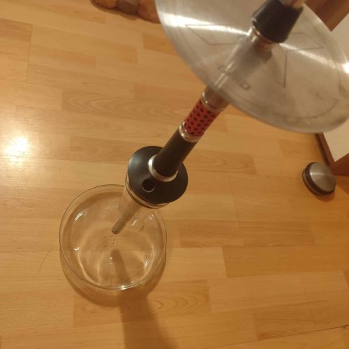 Shisha mit Glasbowl, Metalldeckel und Schlauch auf Holzboden.