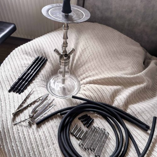 Verschiedene Shisha-Teile, Glasbowl, Schlauch und Zubehör auf Bett.