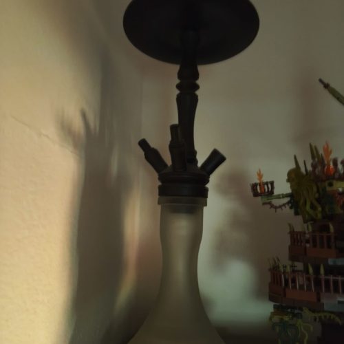 Rauch-Hookah mit dunklem Kopf, auf einem Tisch, mit buntem Schiff im Hintergrund.