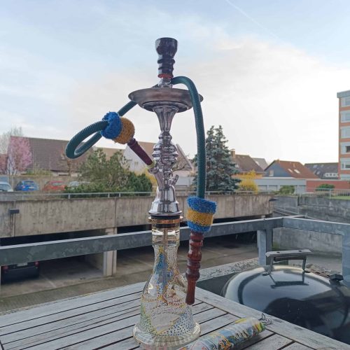 Alte Shisha mit bunten Schläuchen auf Holzterrasse.