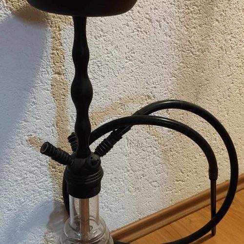Shisha mit Glasbowl, Schlauch und Tabakhalter auf schwarzem Stand.
