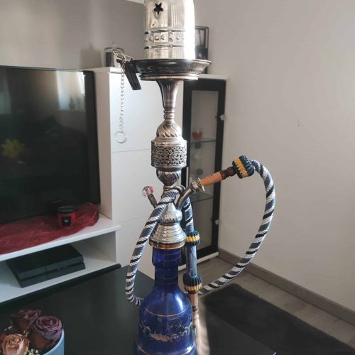 Wasserpfeife mit Wasserbehälter und Schlauch, auf Tisch stehend.