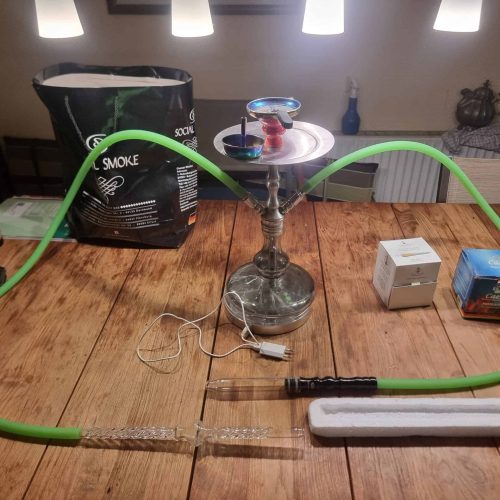 Shisha mit Rauchsäule und Zubehör auf Holztisch.