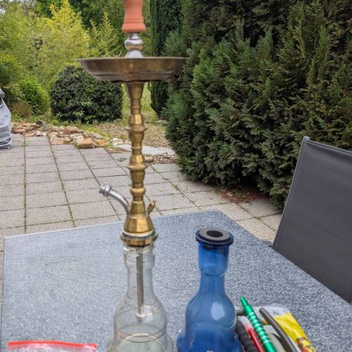 Wasserpfeife auf Gartentisch mit Zubehör, draußen.