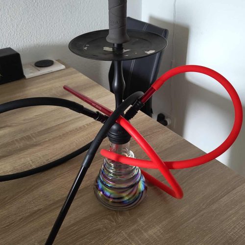 Rauchende Shisha mit buntem Glas und Schlauch auf Holztisch.