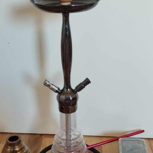 Shisha mit Glasbowl, Schlauch und Zubehör auf Tisch.