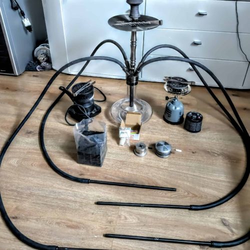 Wasserpfeife mit Schlauch, Tabak und Zubehör auf Holzboden.