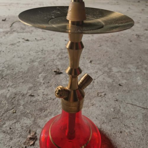 Shisha-Kopf mit goldener Basis auf rotem Glasbehälter, ideal für Wasserpfeifen.