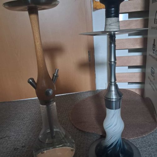 Zwei Wasserpfeifen, eine aus Glas, die andere aus Metall, stehen auf dem Boden.