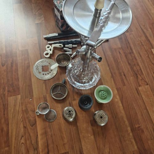 Verschiedene Shisha-Teile und Zubehör auf Holzboden verteilt.