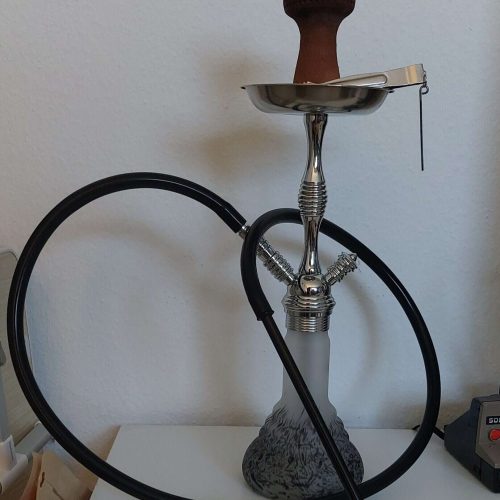 Shisha mit Holkohle, Schlauch und Keramikbasis auf weißem Tisch.