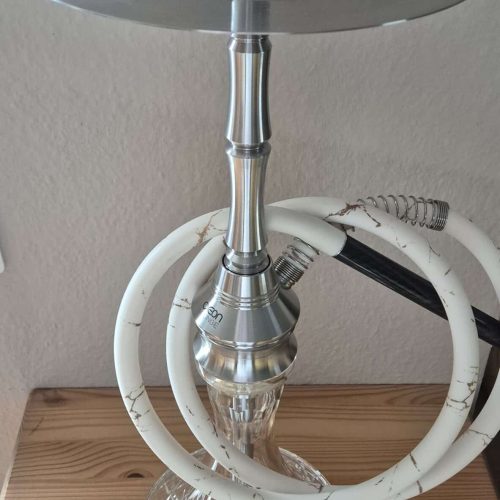 Shisha mit Glasbasis, Metallaufsatz und Schläuchen, auf Holzoberfläche.