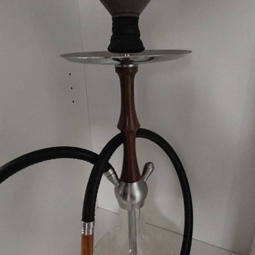 Shisha mit Glasbowl, Schlauch und Metallaufsatz im weißen Regal.