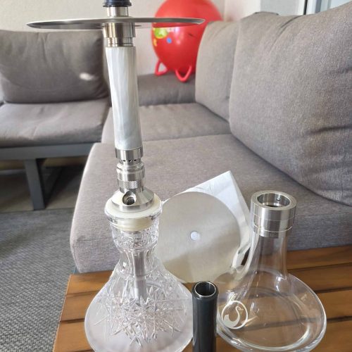 Shisha-Set mit Glasbowl, Metallrohr und Zubehör auf Holztisch.