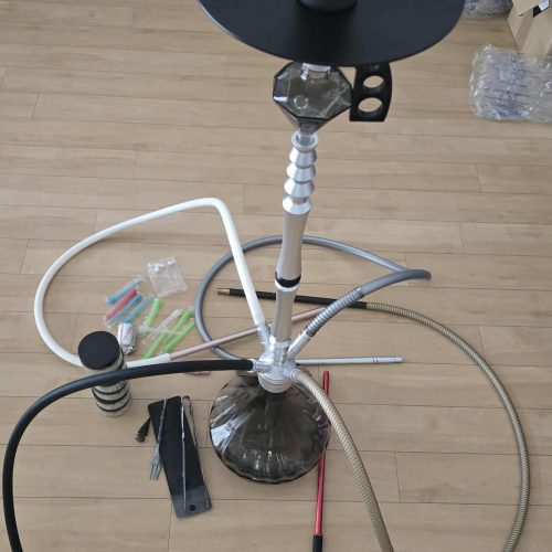 Shisha mit Glasbowl, Schlauch und Zubehör auf Holzboden.