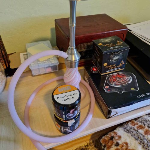 Shisha mit Rauchrohr und Kopf, auf einem Tisch mit Zubehör und Dekoration.