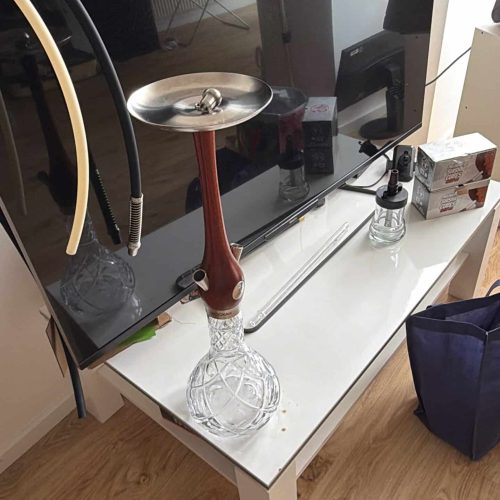 Shisha Glasbowl auf TV-Tisch mit Zubehör und Fernseher im Hintergrund.