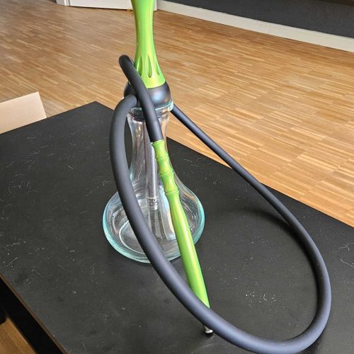 Moderne Shisha mit grüner Rauchsäule und Glasbasis, auf Tisch stehend.
