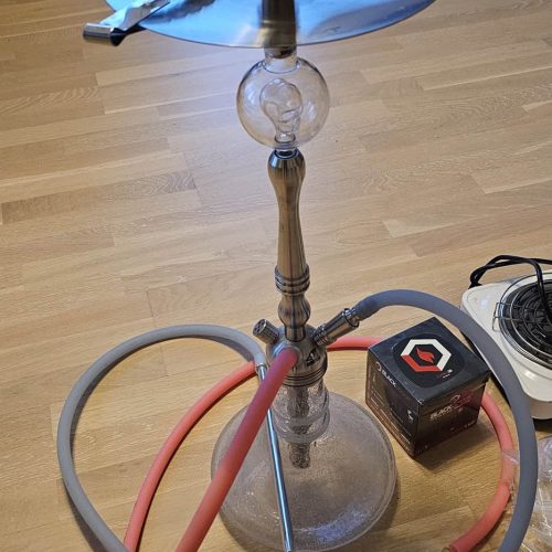 Rauchende Wasserpfeife auf einem Tisch, mit Schlauch und Zubehör sichtbar.