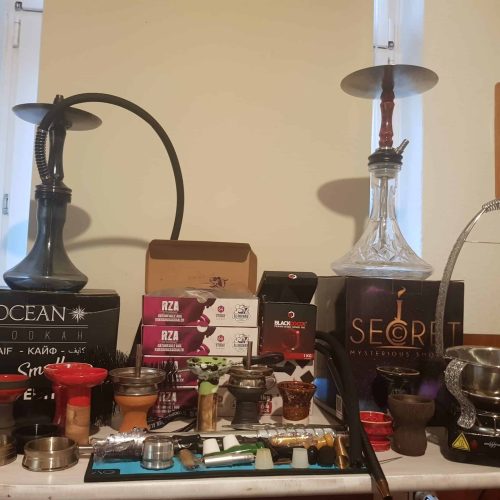 Verschiedene Shisha-Teile, Tabak, Kohle und Zubehör auf einem Tisch.
