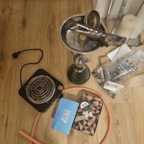 Shisha mit Zubehör, Tabak und Feuerzeug auf Holzboden.