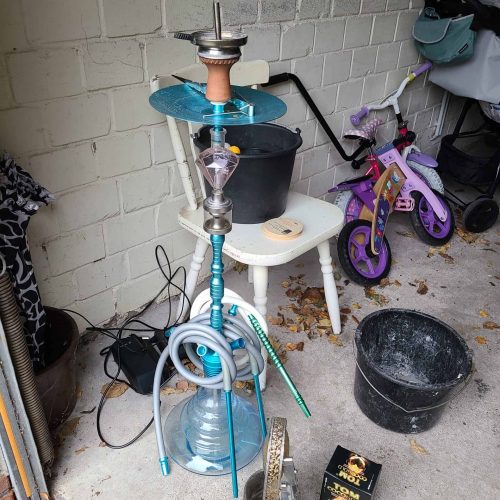 Rauchsäule mit Wasserpfeife, Zubehör, Kinderfahrrad und Dekorationsgegenstände im Außenbereich.