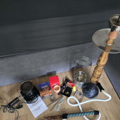 Verschiedene Shisha-Teile, Tabak, Zigaretten und Zubehör auf Holztisch.