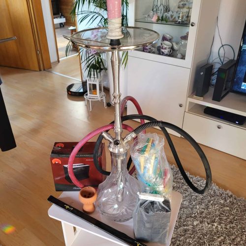 Rauchende Shisha auf einem kleinen Tisch mit Zubehör in einem Wohnzimmer.