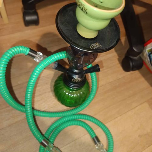 Grüne Shisha mit Glasbowl und Schlauch auf Holzboden.