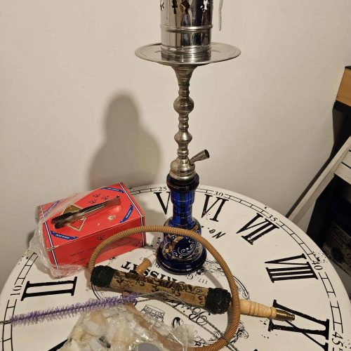 Shisha mit Zubehör auf Tisch, Uhr im Hintergrund.