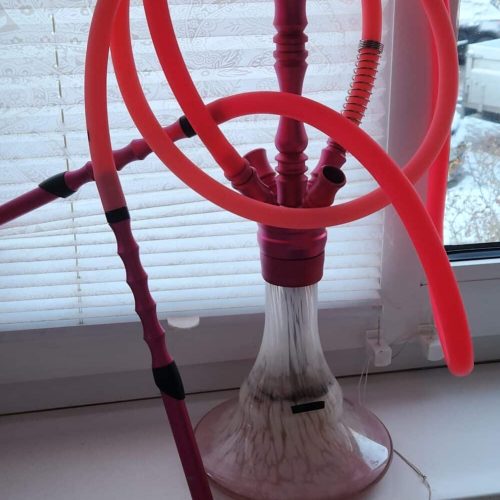 Shisha mit rotem Schlauch und Glasbasis, auf Fensterbank stehend.