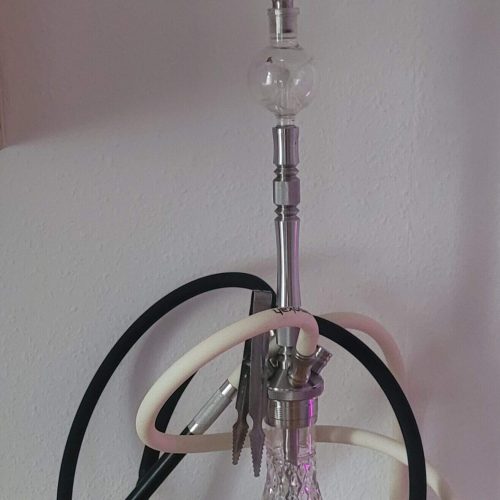Shisha mit Glasgefäß, Schläuchen und Kopf, auf Tisch stehend.