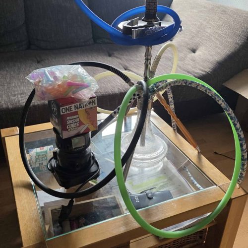 Raucherset mit Wasserpfeife, Schlauch und Zubehör auf Couchtisch.