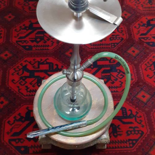 Shisha-Kohleanzünder mit Glasbowl und Schlauch auf rotem Teppich.