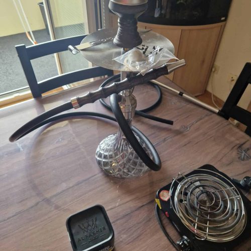 Shisha mit Glasbowl, Schlauch und Heizgerät auf Tisch.