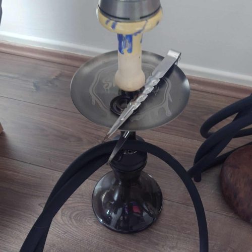 Shisha mit Glasbowl, Schlauch und Zubehör auf Holzboden.