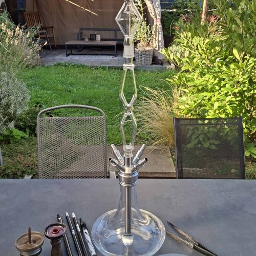 Großer Shisha-Kopf mit Glasbowl, Schlauch und Zubehör auf Tisch.