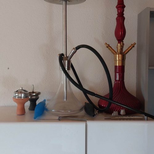 Shisha mit rotem Shishabowl, Metallrohr und Zubehör auf Tisch.