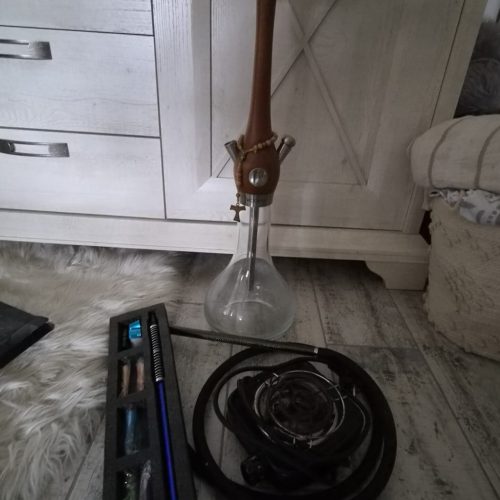 Shisha-Glasbowl mit Schlauch und Zubehör auf Boden.