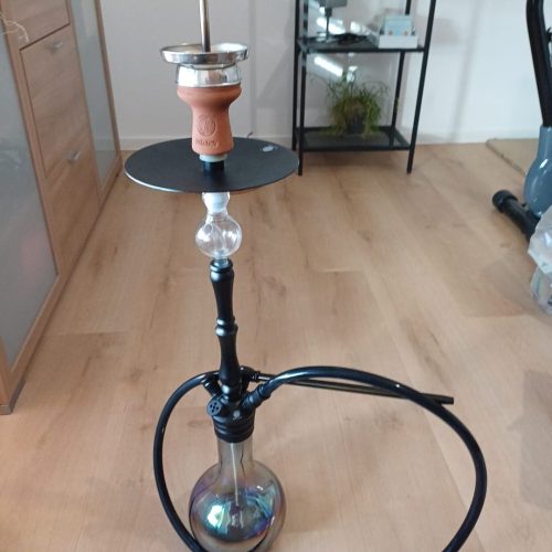 Shisha mit Glasbase, Rauchsäule und Zubehör im Raum.